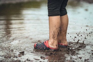 Yağmurdan sonra çamurlu bir su birikintisinde yürüyen çocukların ayakları..