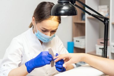 Manikürcü manikürcüde manikür yapıyor. Tırnak törpüsü kullanıyor..