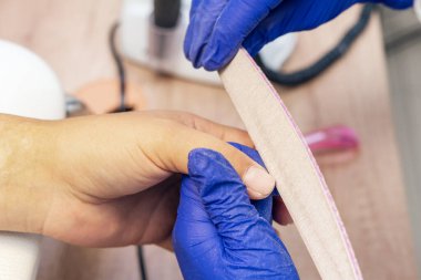 Manikürcü manikürcüde manikür yapıyor. Tırnak törpüsü kullanıyor..