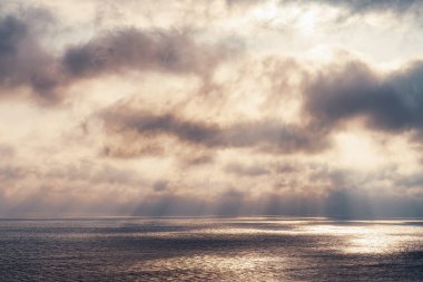 Güneş ışınları denizin üzerindeki dramatik kara bulutlar arasından suyla ışık demetleri oluşturur..