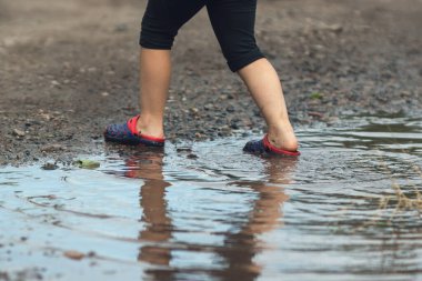 Yağmurdan sonra çamurlu bir su birikintisinde yürüyen çocukların ayakları..