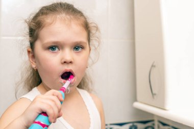 Küçük kız sabah banyoda elektrikli diş fırçasıyla dişlerini fırçalıyor..