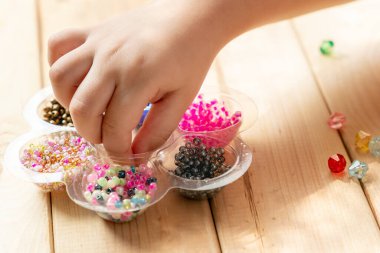 Çocuk kendi elleriyle mücevher yapıyor, ipliğe renkli boncuklar takıyor..