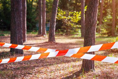 Red and white barrier tape, fenced off dangerous place or crime scene in the forest. clipart