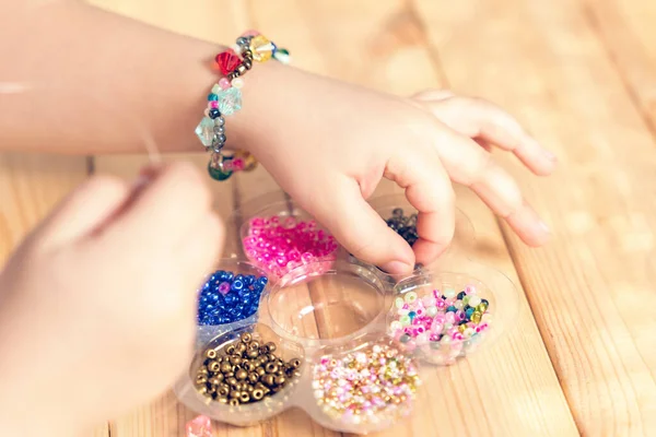 Çocuk kendi elleriyle mücevher yapıyor, ipliğe renkli boncuklar takıyor..
