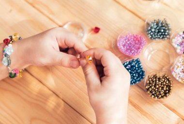 Çocuk kendi elleriyle mücevher yapıyor, ipliğe renkli boncuklar takıyor..