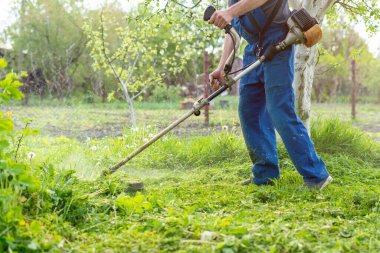 Bahçıvan bahar bahçesinde bir budama makinesiyle çimleri biçer.