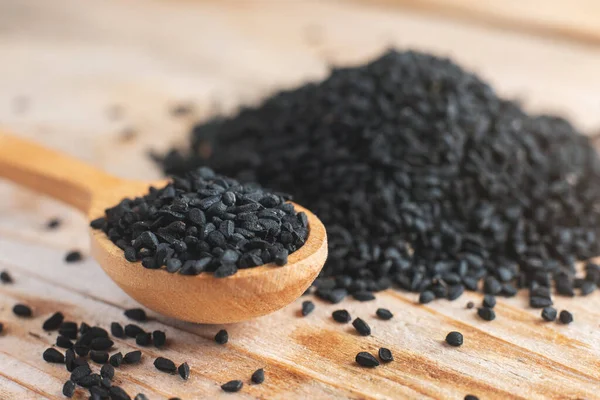 Black cumin seeds on wooden spoon on wooden background.