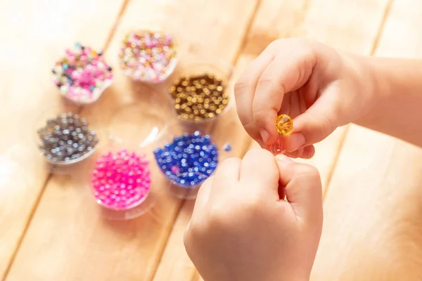 The child makes jewelry with his own hands, stringing colorful beads on a thread.