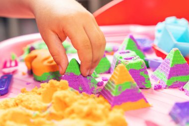 Çok renkli kinetik kumla oynayan bir çocuğun elleri.