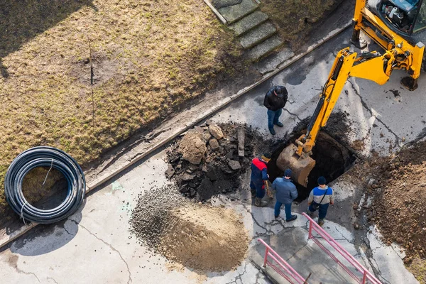 An excavator digs a trench to repair a pipeline on a city street.