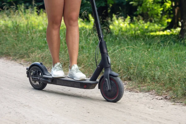 Female feet on an electric scooter riding on a dirt road.