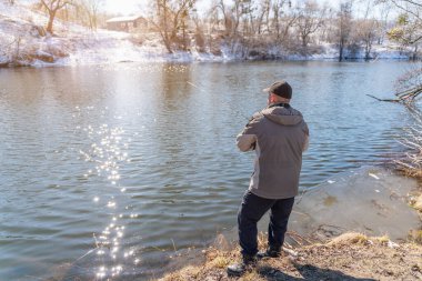 Elinde olta olan bir balıkçı baharın başlarında karla kaplı bir nehrin kıyısında balık yakalar..