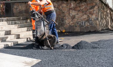 Kaldırımların küçük bölümlerini tamir ederken el arabası kullanarak asfalt karışımı taşıma ve yayma