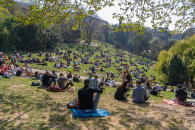 Paris, Fransa - 04 04 04 2021: Park des Buttes Chaumont. Üçüncü tecrit sırasında insanlar parkın çimlerinde oturuyorlar.