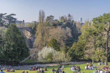 Paris, Fransa - 04 04 04 2021: Park des Buttes Chaumont. Üçüncü tecrit sırasında insanlar parkın çimlerinde oturuyorlar.