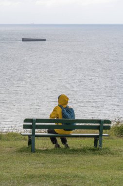 Arromanches-les-Bains, Fransa - 08 03 2021: Sarı yağmurluk ve sırt çantası giyen bir kadın