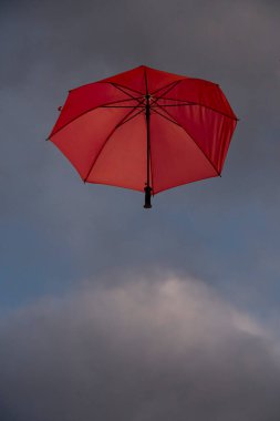 Bulutlu bir gökyüzünde uçan kırmızı açık şemsiye manzarası