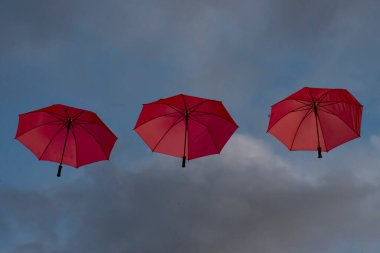 Bulutlu bir gökyüzünde uçan üç kırmızı açık şemsiye manzarası
