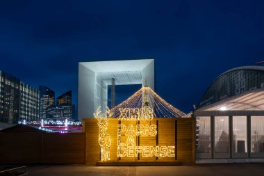 Paris, Fransa - 12: 08 2025: Noel pazarı. Parvis de la Defense 'ın ortasındaki aydınlık Noel geyiğinin panoramik görüntüsü ve geceleri arkadaki binalar.