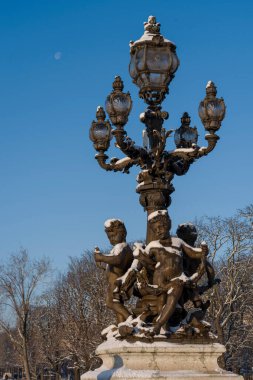 Paris, Fransa - 01 06 2026: kar taneleri. Sokak lambasının detaylı görüntüsü ve Alexander Köprüsü 'ndeki melek heykelleri ve kar ve mavi gökyüzünün altındaki ay.