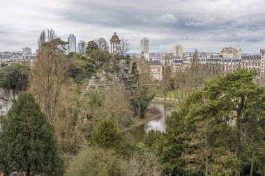 Paris, Fransa - 02 21 2026: Park des Buttes Chaumont. Belvedere adasının panoramik manzarası. Sibyl Tapınağı, göl ve kışın arkasında binalar.