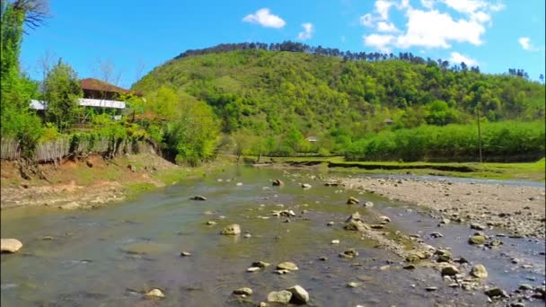 Река течет возле деревни с лесом на холме — стоковое видео