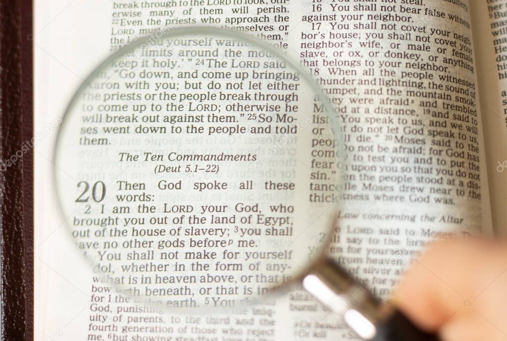 The ten commandments of God Jesus Christ from Exodus 20. Open Holy Bible with human hand holding a magnifying glass. Biblical concept. Spiritual intent Law of God. Truth and faith in God's Word.