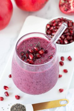 Pomegranate and chia seed smoothie in a glass with fresh fruit on white kitchen table.