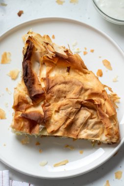 Mutfak masasında yoğurt bulunan bir tabak ev yapımı Burek. Üst Manzara. Geleneksel Balkan yemekleri.