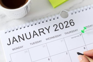1 Ocak 2026 yeni yıl takviminde kahve fincanı ve yapışkan notlarla beyaz masa üzerinde bir broş olacak. İş hedefleri hatırlatma, yıllık planlama konsepti. Üst görünüm.