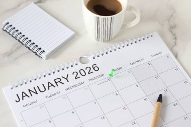 1 Ocak 2026 yeni yıl takvimine göre kahve fincanı ve not defteriyle beyaz mermer zemin üzerinde bir broş. İş hedefleri anımsatıyor, kararlar, yıllık planlama kavramı.