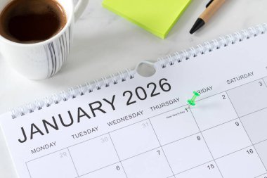 2026 Yeni Yıl takvimi, ocak ayının ilk randevusu kahve fincanı ve yapışkan notlarla beyaz bir masa üzerinde. İş hedefleri anımsatıyor, yıllık planlama kavramı.