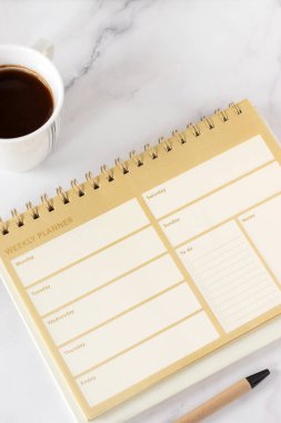 Günlük notları olan haftalık planlamacı ve beyaz mermer arka planda kahve fincanı olan boş sayfaları listelemek. Üst Manzara. Kişisel hedefler, hedefler, çözümler ve zaman yönetimi kavramı.