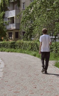 Siyah kotlu ve beyaz tişörtlü bir adam sokakta yürüyor. Arka görünüm. 