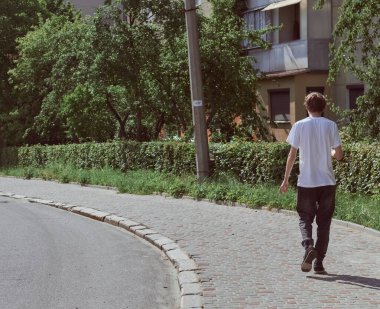 Siyah kotlu ve beyaz tişörtlü bir adam sokakta yürüyor. Arka görünüm. 