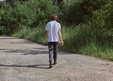 Siyah kot ve beyaz tişörtlü bir adam parkta yolda yürüyor..