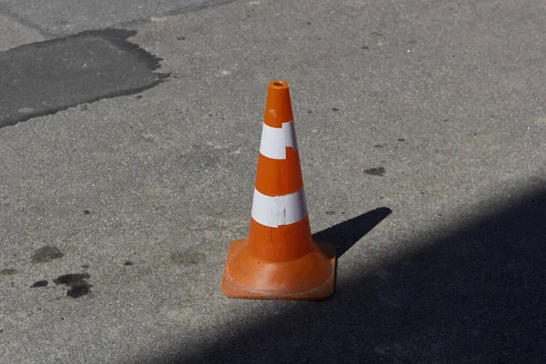 Orange traffic cone placed on the asphalt street. Warning sign on road. Orange warning sign in white stripe