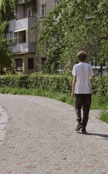 Siyah kotlu ve beyaz tişörtlü bir adam sokakta yürüyor. Arka görünüm. 