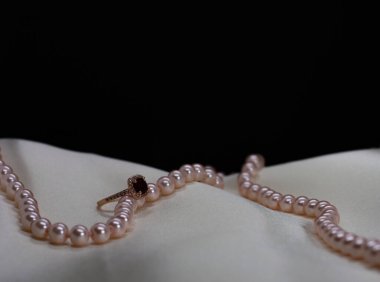 Beyaz yüzeyinde pembe inci kolyesi olan küçük elmaslı Altın Mücevher Yakut yüzüğü. Siyah arkaplan