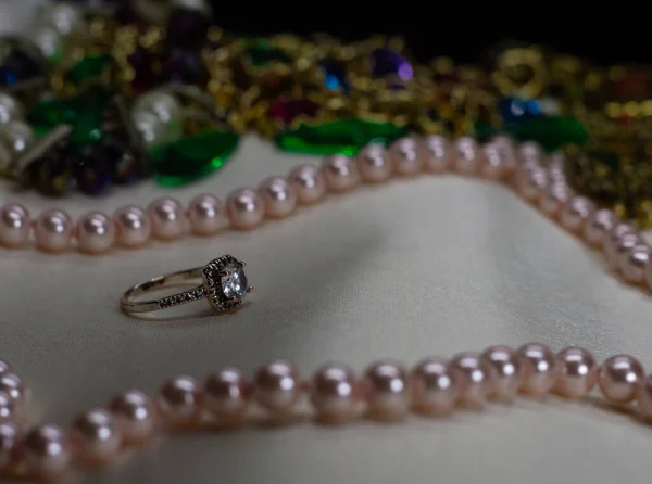 Beyaz yüzeyinde pembe inci kolyesi olan küçük elmaslı Altın Mücevher yüzüğü. Altın ve Mücevherler arka planda bulanıklaştı, Siyah arkaplan