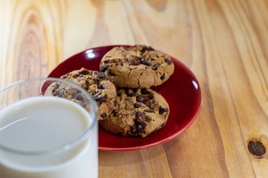Kırmızı tabakta çikolatalı kurabiye ve tahta masada süt - alan alanını kopyala