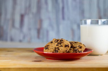 Kırmızı tabakta çikolatalı kurabiye ve tahta masada süt - alan alanını kopyala