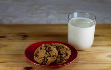 Kırmızı tabakta çikolatalı kurabiye ve tahta masada süt - alan alanını kopyala