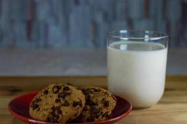 Kırmızı tabakta çikolatalı kurabiye ve tahta masada süt - alan alanını kopyala