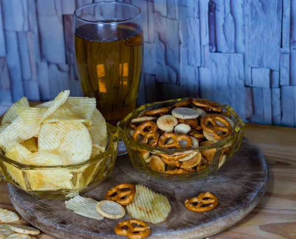 Cold beer and wavy potato chips in a bowl and salty snacks pretzel on a wood table