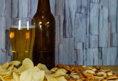 Soğuk bira ve dalgalı patates cipsi kasede ve ahşap masada tuzlu çerezler.