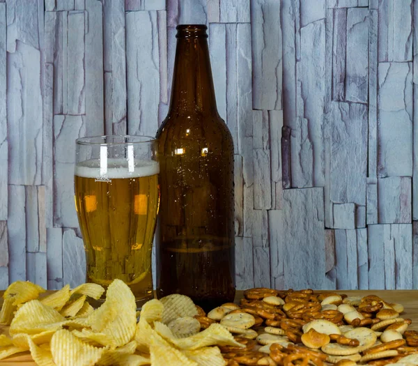 Soğuk bira ve dalgalı patates cipsi kasede ve ahşap masada tuzlu çerezler.