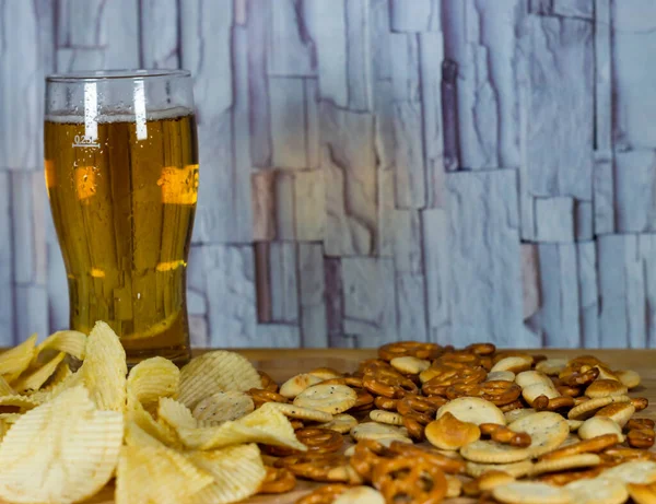 Cold beer and wavy potato chips in a bowl and salty snacks pretzel on a wood table