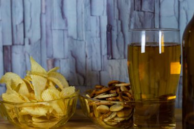 Soğuk bira ve dalgalı patates cipsi kasede ve ahşap masada tuzlu çerezler.
